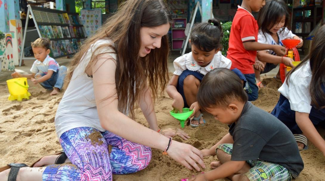 A high school student volunteering abroad under 18 plays in the sand with a young boy in Cambodia. A volunteers spends time with the children in Cambodia after joining volunteering opportunities for high school students with Projects Abroad.